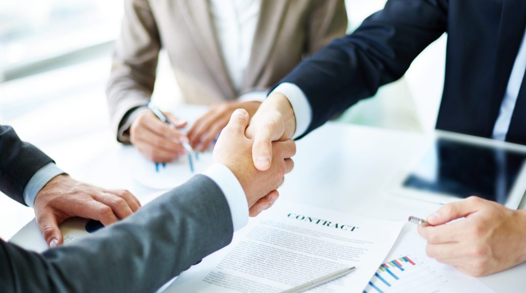 Image of business partners handshaking over business objects on workplace