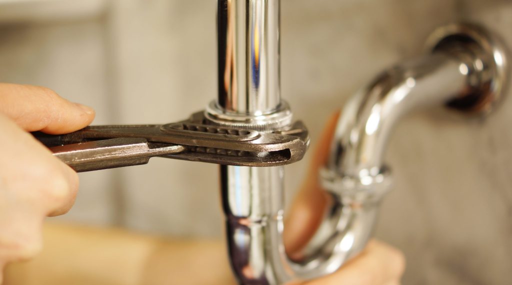 Plumbing repair service. Professional installer with spanner checking pipe.